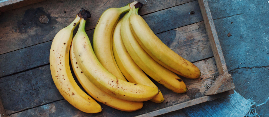 Bandeja de madera sobre superficia azul. Manojo de bananos.