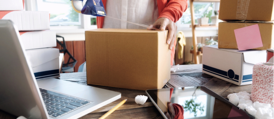 Mujer atendiendo negocio de venta en línea. Cajas y computadora.